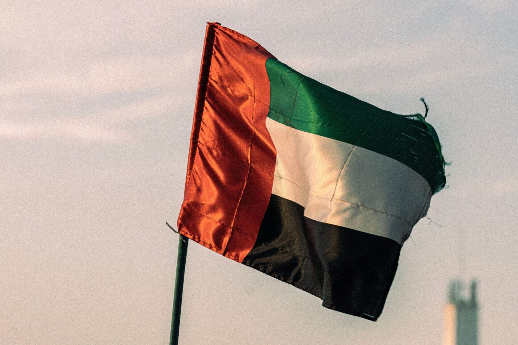 United Arab Emirates flag fluttering in a Dubai urban setting, captured during the day.